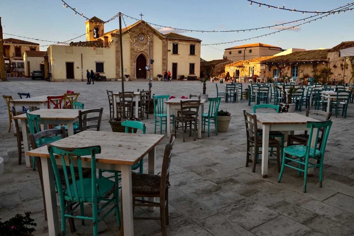 Scorcio dei vicoli di Marzamemi con decorazioni floreali, botteghe artigiane e la luce del sole che filtra tra le case